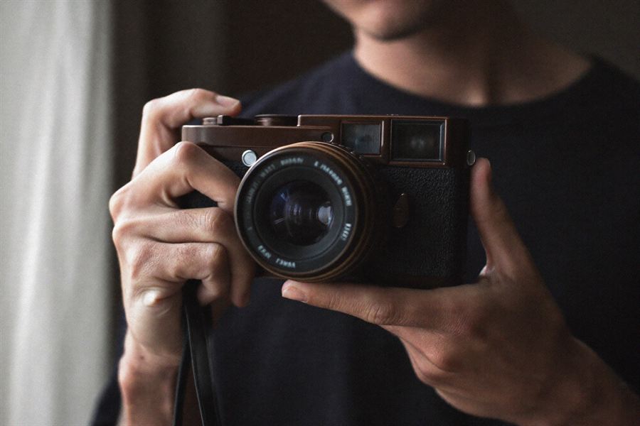 A photographer holding a 35mm film camera at chest height in soft window light.