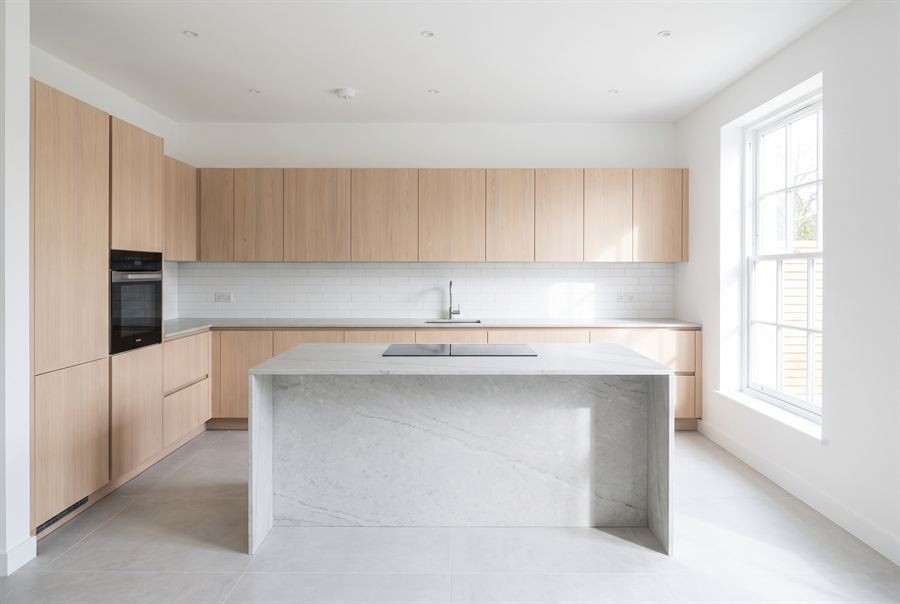 A modern kitchen with pale oak cabinetry and a large stone island in bright daylight.