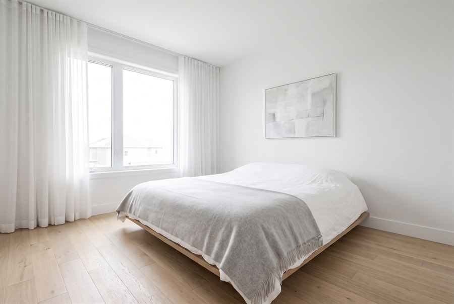 A principal bedroom with a low platform bed, white linen and pale oak floor.