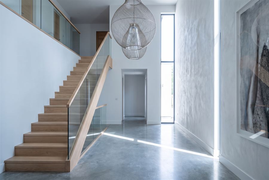 A double-height entrance hall with a pale oak staircase and a shaft of daylight across the wall.